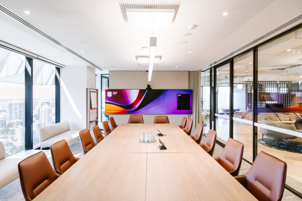 Modern executive boardroom at Bentleys Queensland with large timber conference table, brown leather chairs, and vibrant digital display screen overlooking Brisbane