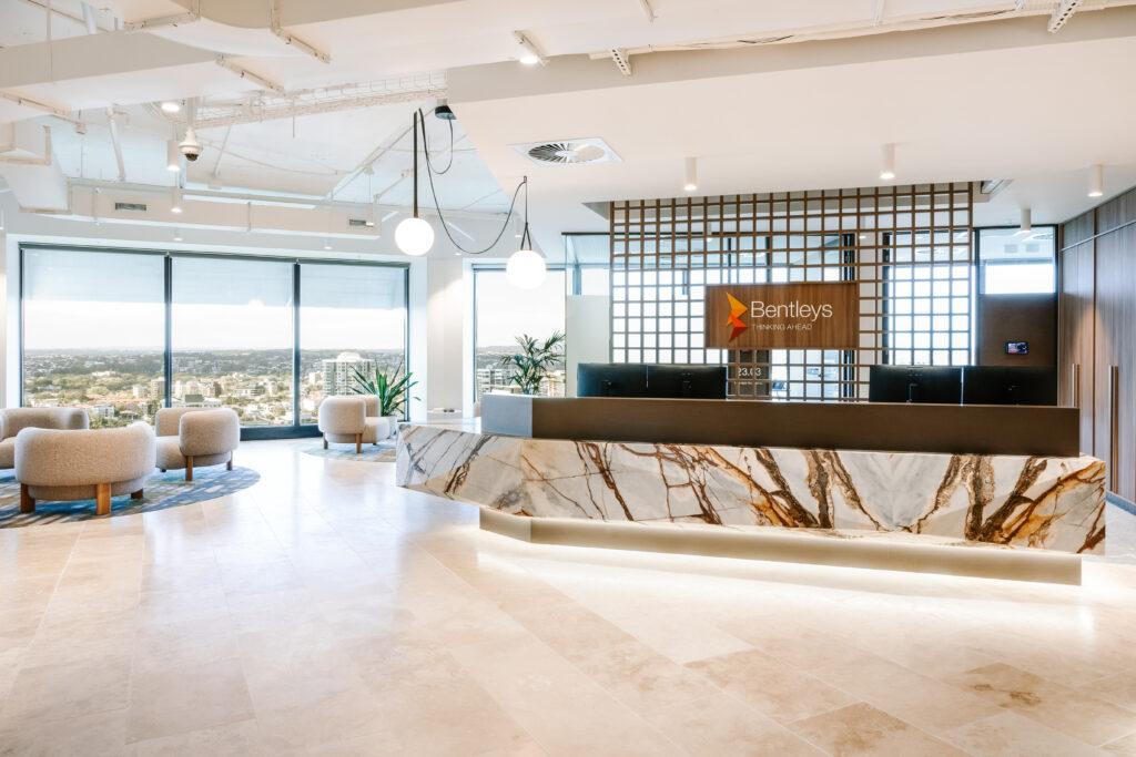 Wide view of Bentleys Queensland reception area with marble desk, client waiting lounge, and panoramic Brisbane city views