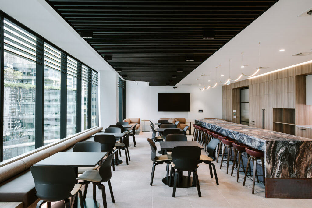 Spacious modern cafe and breakout zone in Dentons Brisbane office with marble bar counter, high stools, dining tables, and large windows overlooking the city.
