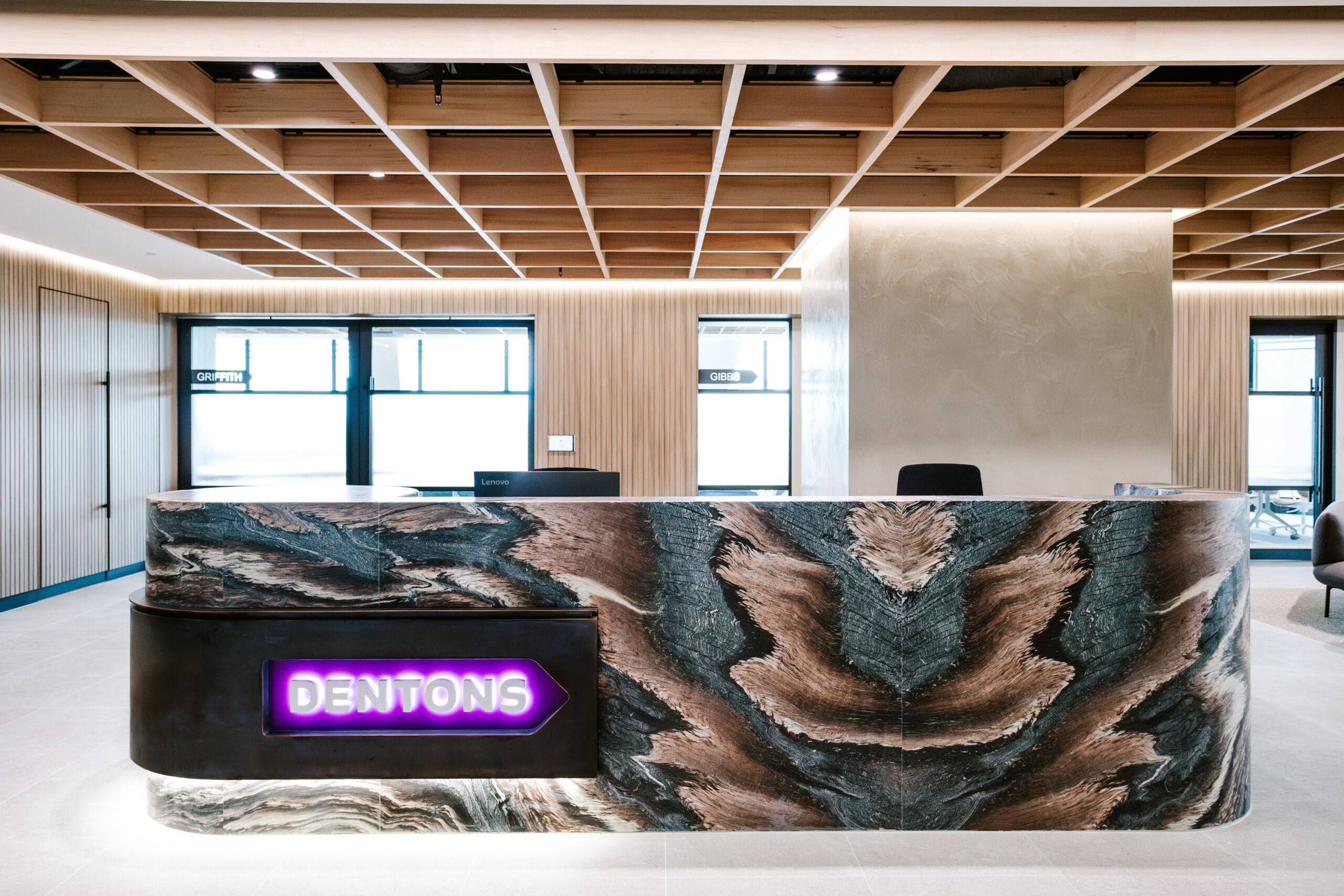 Hero view of the premium reception desk with dramatic veined marble and illuminated Dentons signage in the Brisbane office.