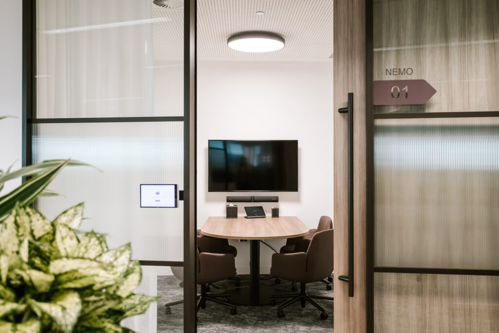 Modern glass-walled meeting room named NEMO 01 in Dentons Brisbane office, featuring a round wooden table, video conferencing setup, and ergonomic seating.